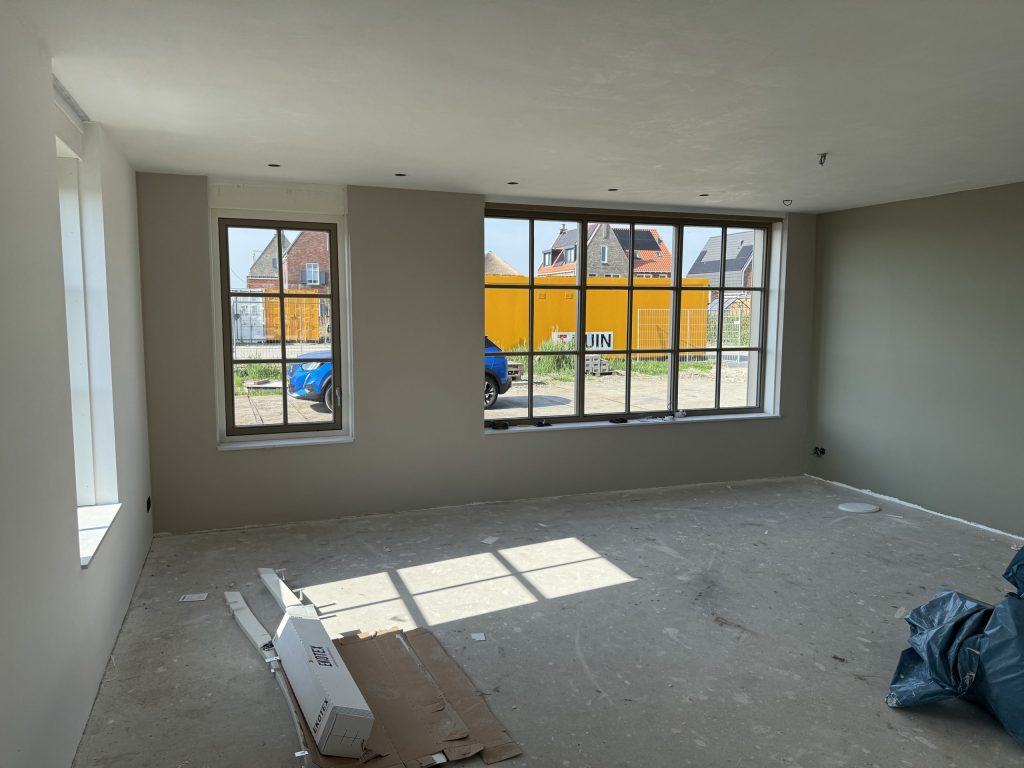 Nieuw opgeleverde woonkamer met grote roedenramen en wanden in een zachte grijsgroene kleur